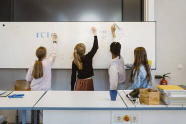 Female students writing on whiteboard in classroom - MASF38321