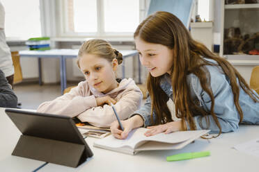 Curious schoolgirls doing E-learning through tablet PC sitting at desk in classroom - MASF38334