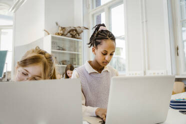 Schoolgirl using laptop sitting at desk in classroom - MASF38335