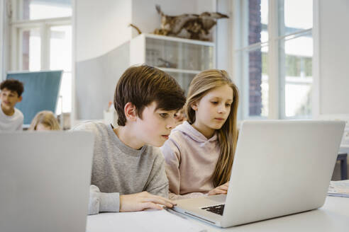 Concentrated boy watching laptop with female friend at desk in classroom - MASF38338