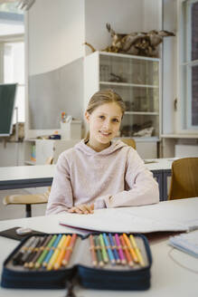 Porträt einer lächelnden Schülerin am Schreibtisch im Klassenzimmer - MASF38340