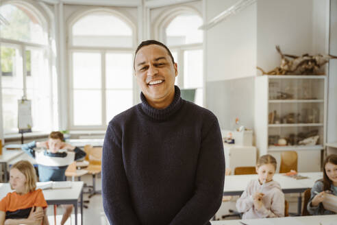 Porträt eines glücklichen männlichen Lehrers, der im Klassenzimmer steht - MASF38351