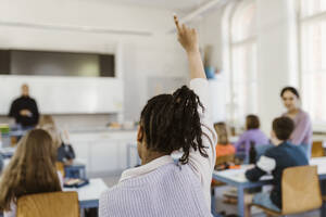 Rear view of female student raising hand during lecture in classroom - MASF38365