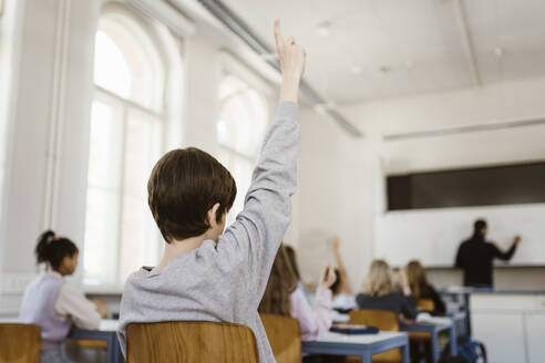 Boy raising hand while attending lecture in classroom - MASF38366