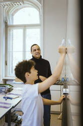 Male teacher looking at student writing on whiteboard in classroom - MASF38375