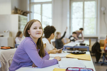 Porträt einer lächelnden Schülerin am Schreibtisch im Klassenzimmer - MASF38378