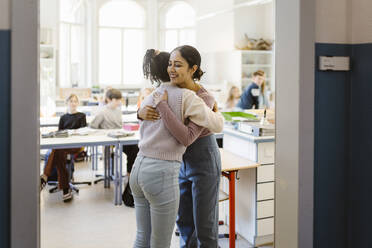 Schoolgirl embracing female teacher standing in classroom - MASF38391