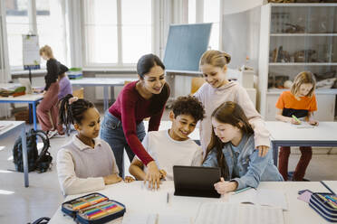 Teacher with male and female students using tablet PC at desk in classroom - MASF38403