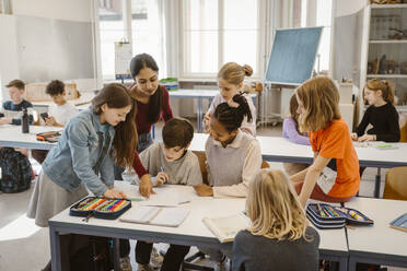 Female teacher assisting students learning together in classroom - MASF38407