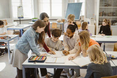 Teacher explaining multiracial students at desk in classroom - MASF38408