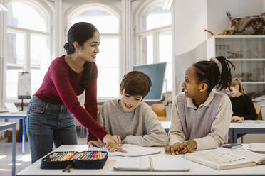 Happy teacher looking at female student while assisting in classroom - MASF38410