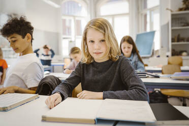 Porträt eines Schuljungen mit blondem Haar, der am Schreibtisch im Klassenzimmer sitzt - MASF38418