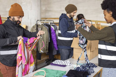 Male and female workers sorting recycled clothes on table at recycling center - MASF38434