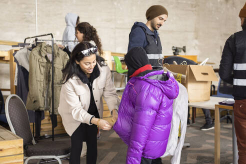 Frau hilft ihrem Sohn mit wattierter Jacke im Recyclingzentrum - MASF38436