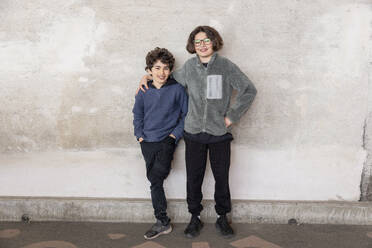 Porträt von lächelnden Brüdern, die im Recyclingzentrum an der Wand stehen - MASF38442