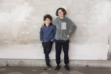 Portrait of smiling brothers standing against wall at recycling center - MASF38442