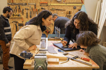 Female technician explaining smart phone repair to mother and son at recycling center - MASF38474