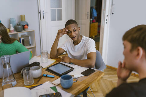 Smiling man looking at friend while studying together - MASF38523