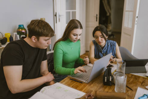 Young friends using laptop while doing school assignment together at home - MASF38531