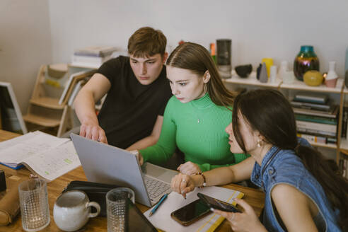 Young friends doing school assignment together while using laptop at home - MASF38532