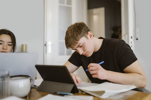 Young man writing while doing homework by friend at home - MASF38536