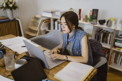 Junge Frau, die einen Laptop benutzt, während sie eine Schulaufgabe zu Hause erledigt - MASF38537