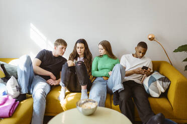 Young multiracial friends using smart phones while sitting together on sofa at home - MASF38538