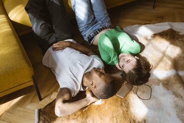 High angle view of smiling man and woman lying on floor at home - MASF38546
