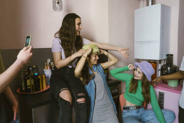 Smiling young female friends enjoying with hats in kitchen at home - MASF38561