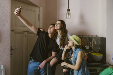 Young man taking selfie with smiling female friends in kitchen at home - MASF38562