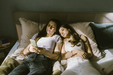 High angle view of young women sharing smart phone while lying on bed at home - MASF38575