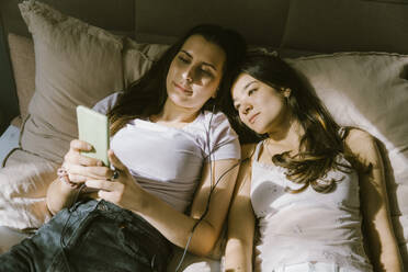 Young women sharing smart phone while lying on bed at home - MASF38576