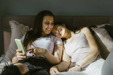 Happy of young women sharing smart phone while lying on bed at home - MASF38577
