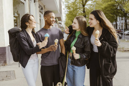 Happy young friends eating ice creams at sidewalk - MASF38582