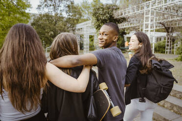 Smiling young man looking back while walking with friends in city - MASF38585