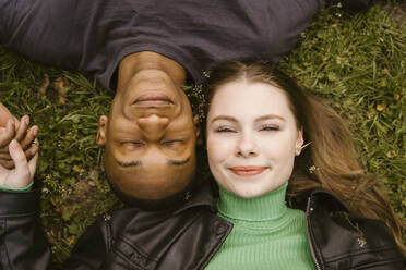 Directly above view of smiling young woman and man lying on grass - MASF38590