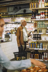 Senior man holding basket and bottle shopping at convenience store - MASF38600