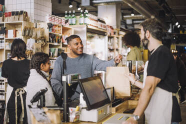 Male retail clerk giving shopping bag to customers at checkout in grocery store - MASF38623