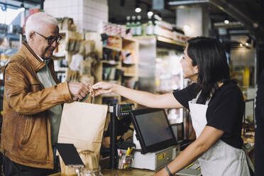 Smiling saleswoman giving shopping bag to senior male customer at store checkout - MASF38625