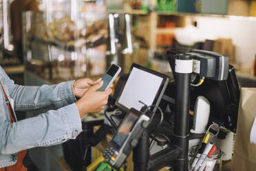 Midsection of woman using smart phone while scanning QR code for payment at store checkout - MASF38627