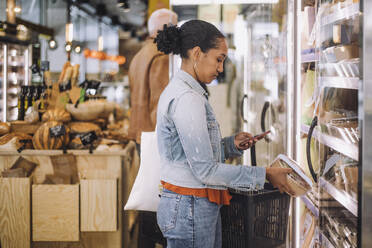 Side view of female customer photographing package while standing at grocery store - MASF38630