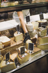 Midsection of female retail clerk removing cheese from display cabinet at grocery store - MASF38634