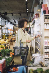 Smiling young male customer using digital tablet mounted on wall at grocery store - MASF38639