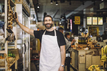 Portrait of smiling male retail clerk standing by rack at organic grocery store - MASF38645