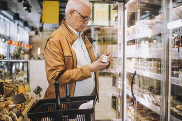 Senior man analyzing container at grocery store - MASF38651