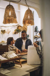 Father and daughter looking at each other while saleswoman packing bag in store - MASF38661