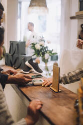 Cropped hands of customer and retail clerk with smart phone at checkout in boutique - MASF38665