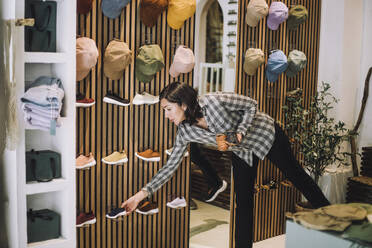 Saleswoman bending over while arranging shoes on display rack at fashion boutique - MASF38666