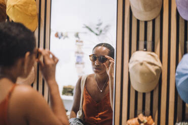 Woman trying sunglasses while looking at reflection in fashion boutique - MASF38669