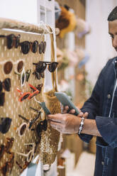 Man photographing label on sunglasses at rack in fashion store - MASF38671